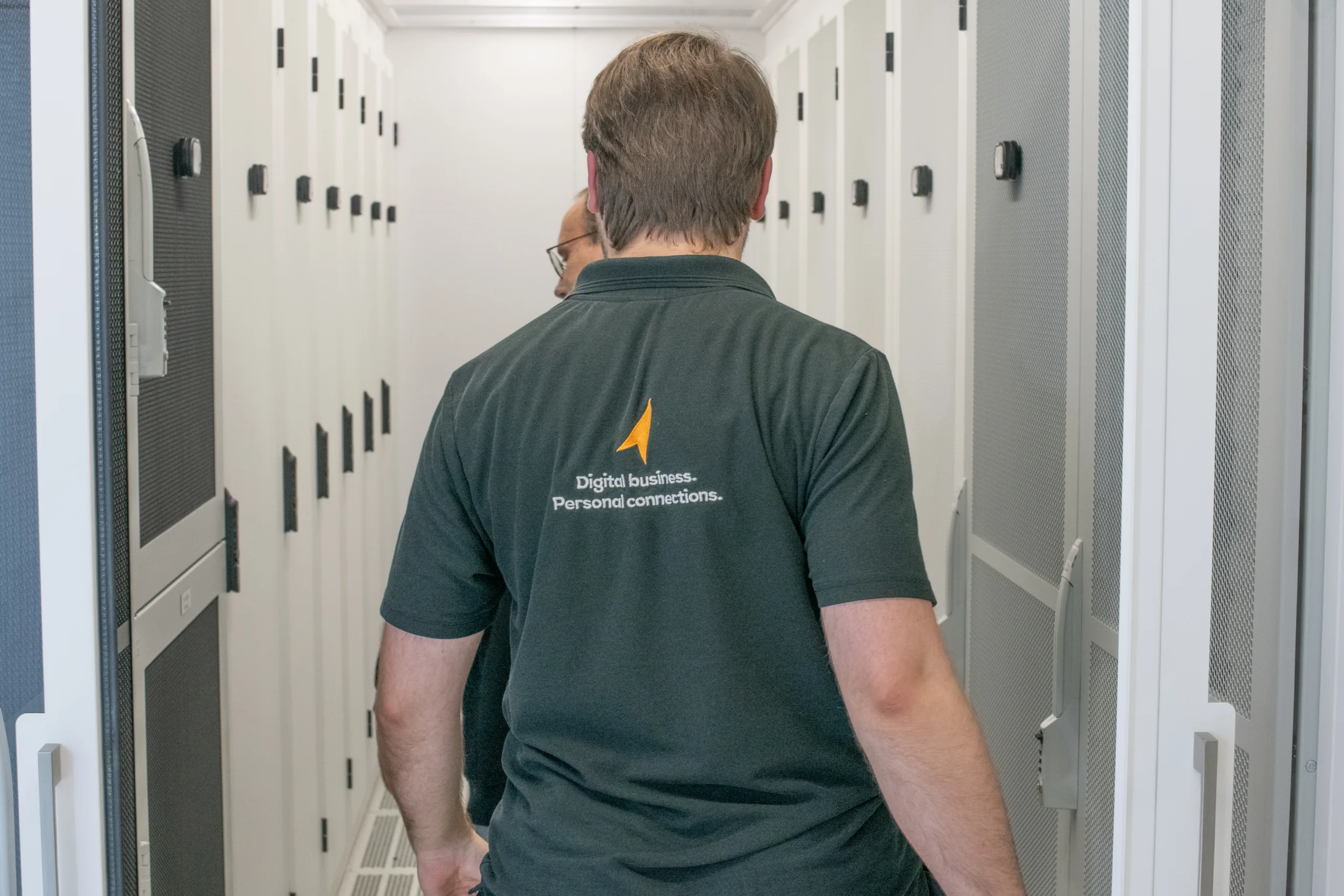 Un homme est dans un centre de données. Il est de dos et on lit sur son polo noir : "Digital business. Personnal Connections.", en dessous du logo de NorthC.